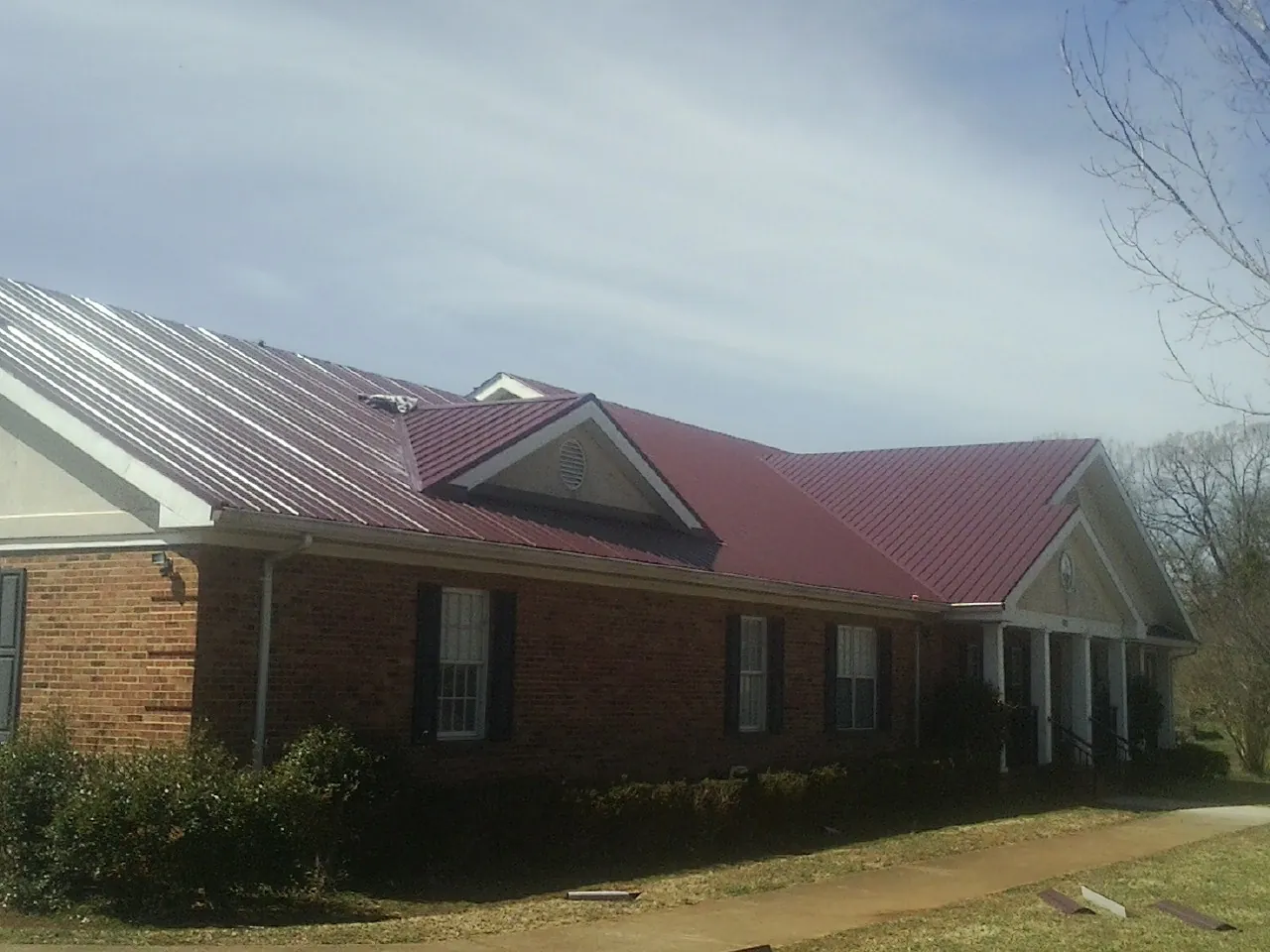 Red metal roof with gabled entries on a long brick building, from a Hail Damage Roof Repair job in Mattawana