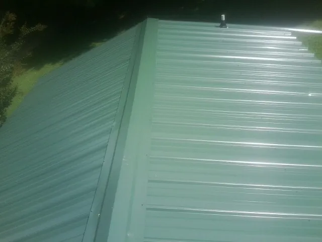 New green metal panels meeting at the ridge of a roof — Flat Roof Repair work by our crew in Mattawana