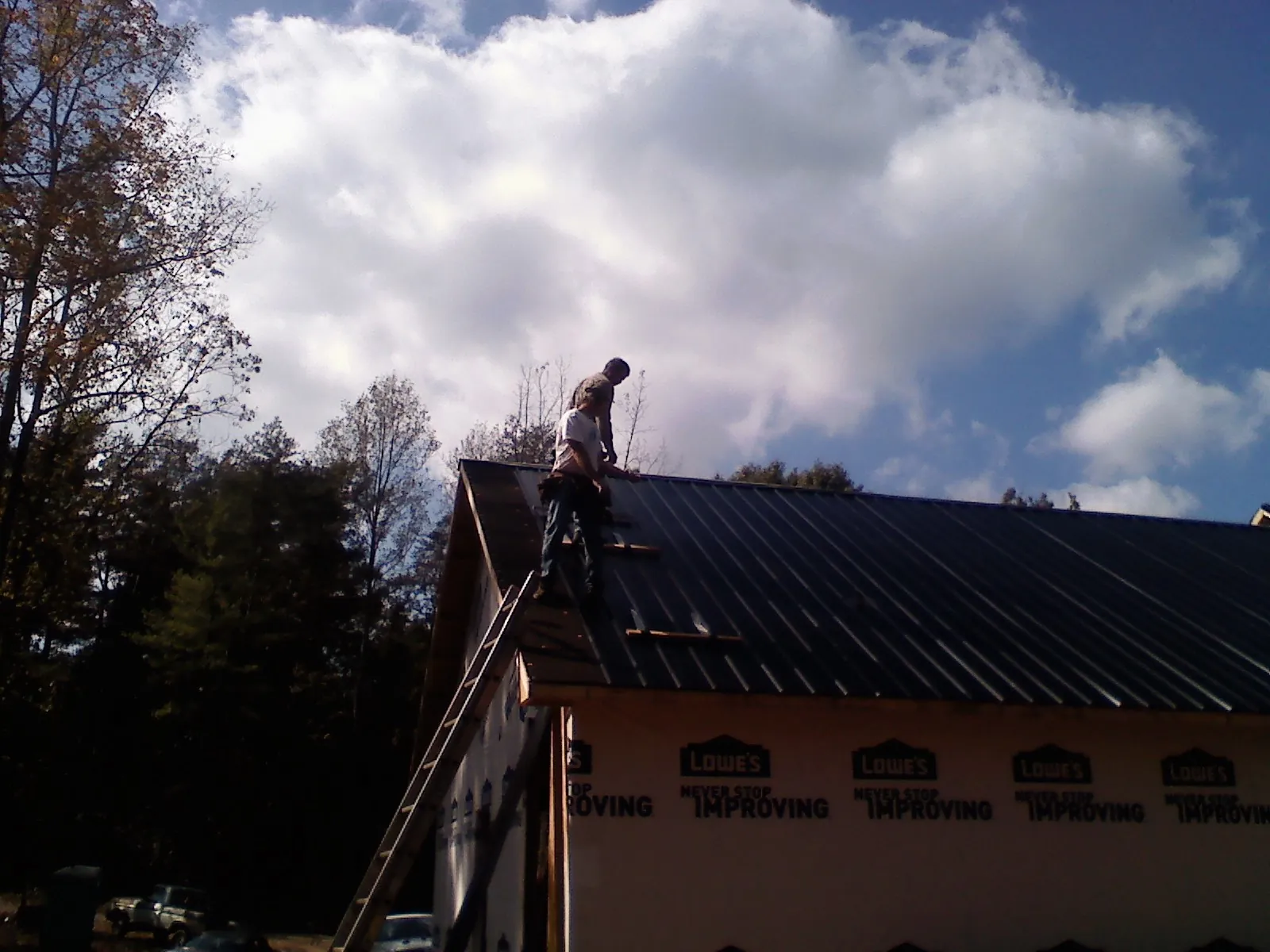 Roofer fastening dark metal panels high against a cloudy sky, from a Roof Inspection job in Mattawana