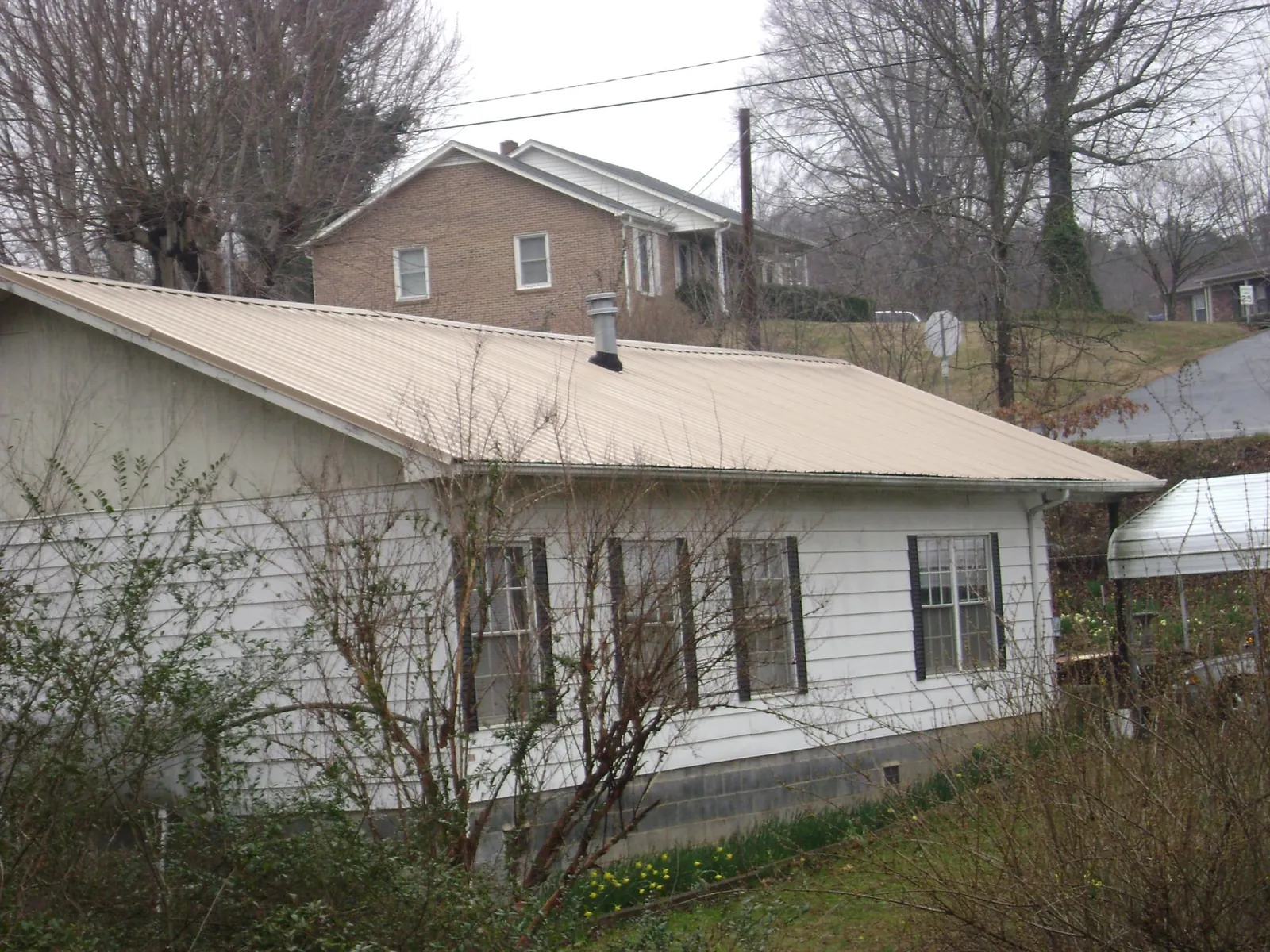 Tan metal roof on a white sided house set into a hillside — Commercial Roofing by Roofing Brothers in Mattawana
