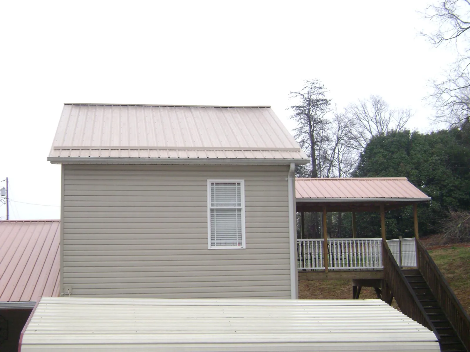 Tan metal roofs on a two story addition and attached porch, from a Roof Replacement job in Mattawana